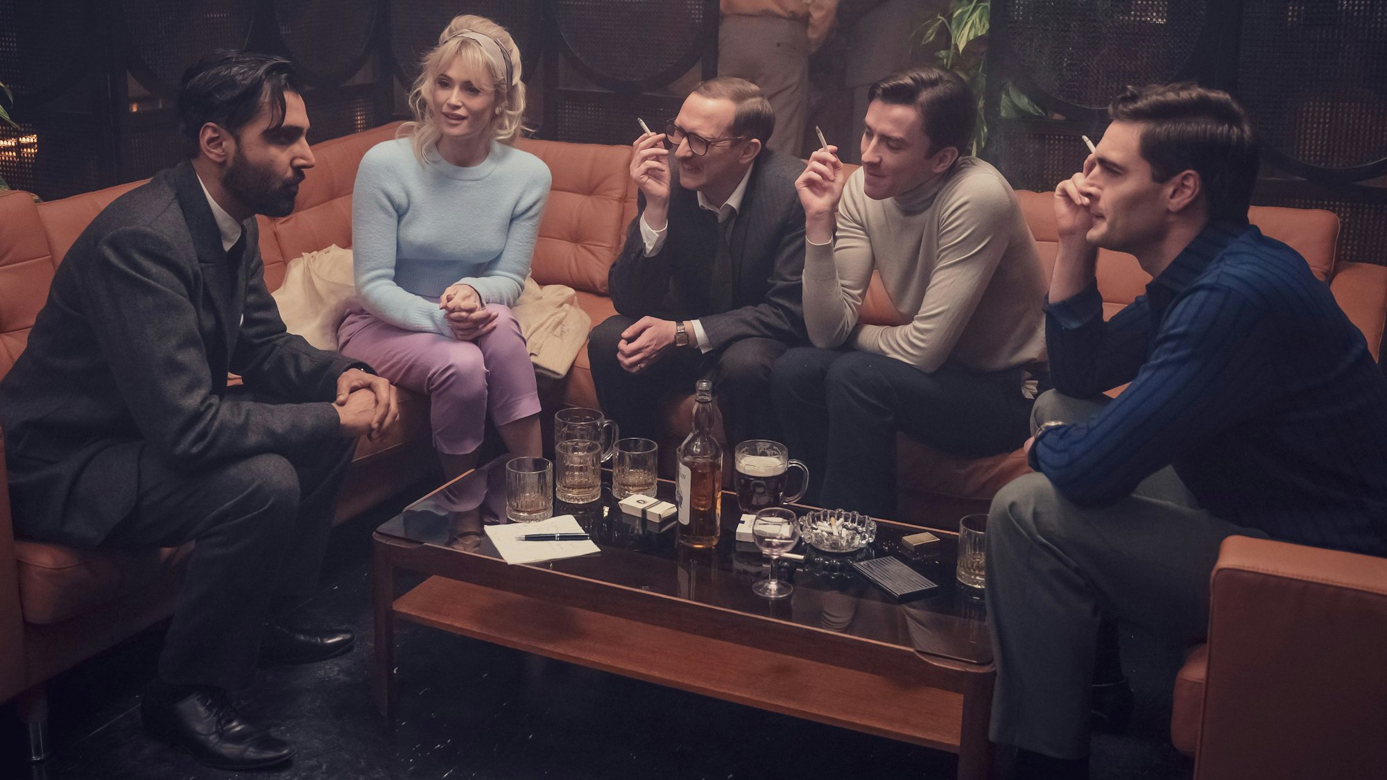 Vier Männer und eine Frau sitzen rauchend auf einem Sofa.