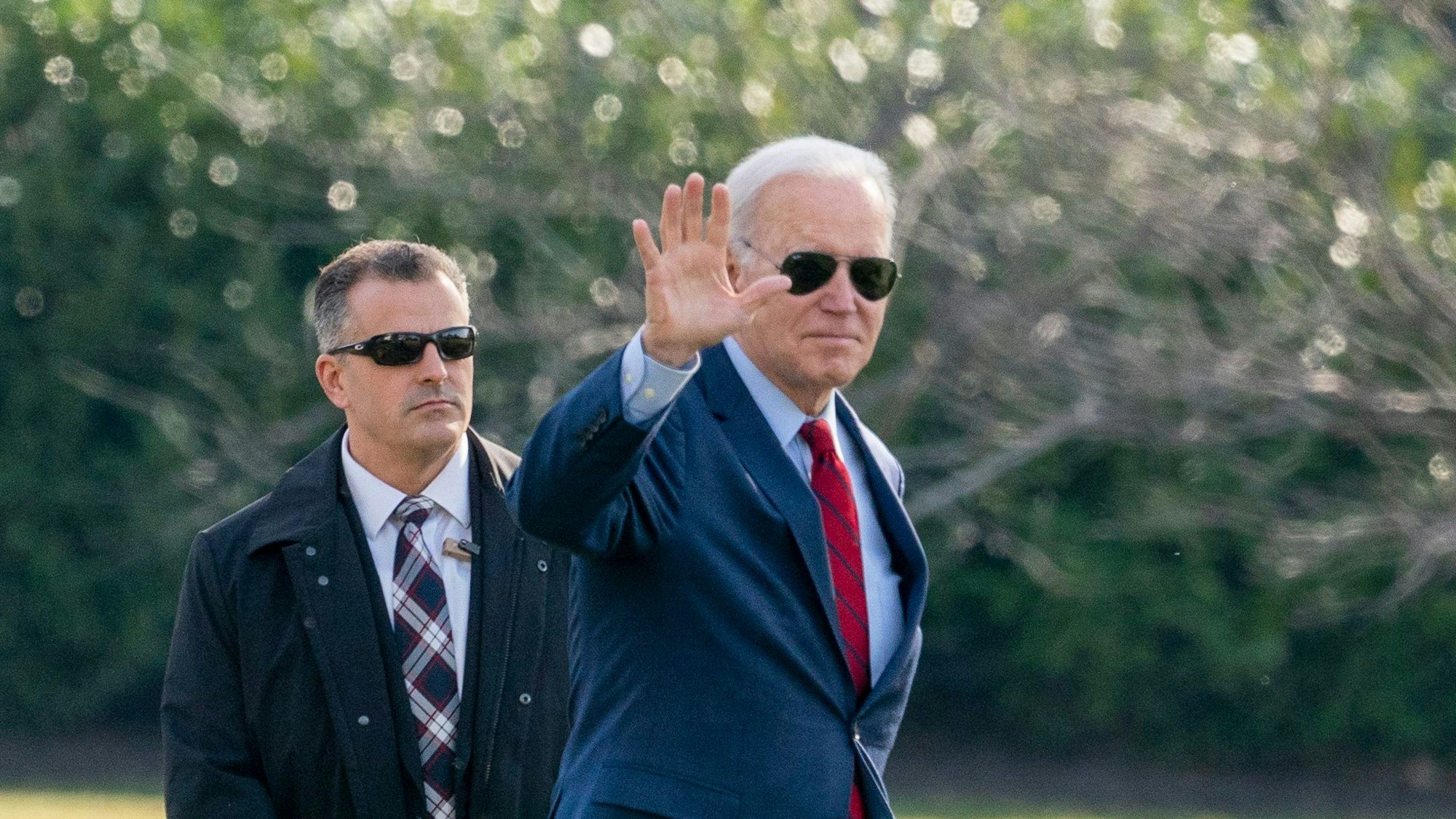 Präsident Joe Biden trägt eine Sonnenbrille und winkt in die Kamera.