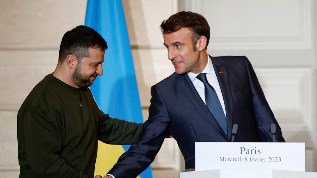 Emmanuel Macron (r), Präsident von Frankreich, und Wolodymyr Selenskyj, Präsident der Ukraine, geben sich vor einer gemeinsamen Pressekonferenz mit Bundeskanzler Scholz (nicht im Bild) die Hand.