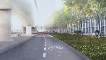 Ein Fahrstreifen mit dem Piktogramm für Radfahrer ist zu sehen. Links sind die Stelzen der Hochbahn, rechts ein Grünstreifen, dahinter ein Gebäude.