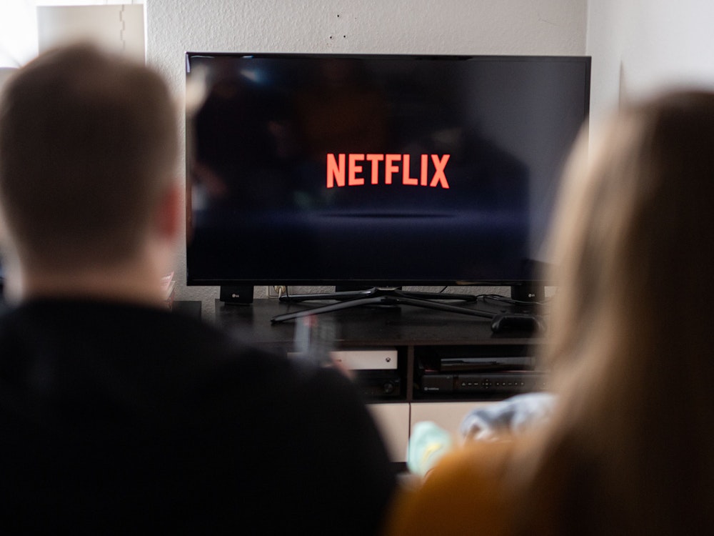 Ein Paar sitzt vor dem Fernseher, auf dem das Netflix-Logo zu sehen ist.