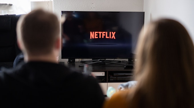 Ein Paar sitzt vor dem Fernseher, auf dem das Netflix-Logo zu sehen ist.