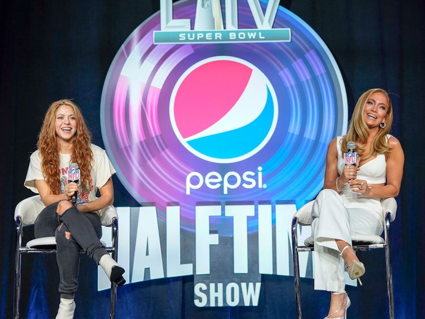 Das undatierte Foto zeigt die beiden Sängerinnen Shakira und Jennifer Lopez. Sie sitzen nebeneinander auf einer Bühne, zwischen ihnen steht das Pepsi-Logo.