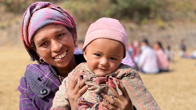 Eine Mutter hält ihr Kleinkind im Arm. Beide schauen und lachen in die Kamera.