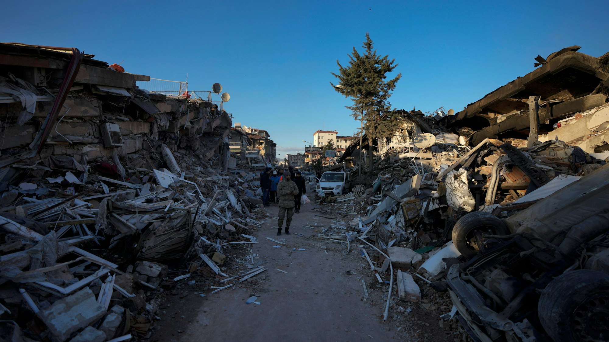 Ein Mann geht inmitten zerstörter Gebäude. In den Erdbeben-Gebieten in Syrien und der Türkei werden bei der Suche nach Verschütteten immer mehr Leichen aus den Resten eingestürzter Gebäude geborgen.