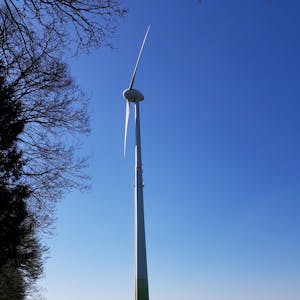 Die Flügel einer Windkraftanlage sind vor blauem Himmel zu sehen.