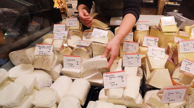 Eine Mitarbeiterin sortiert an der Käsetheke verschiedene Sorten Käse.