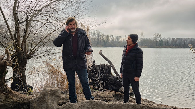 Die Kommissare Franziska Tobler (Eva Löbau) und Friedemann Berg (Hans-Jochen Wagner) stehen am Ufer eines Sees. Vor ihnen ist Erde aufgeschüttet.