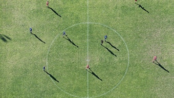 Blick von oben auf einen Fußballplatz, auf dem Fußballer stehen. Im Mittelpunkt ist der Mittelkreis.