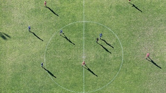 Blick von oben auf einen Fußballplatz, auf dem Fußballer stehen. Im Mittelpunkt ist der Mittelkreis.