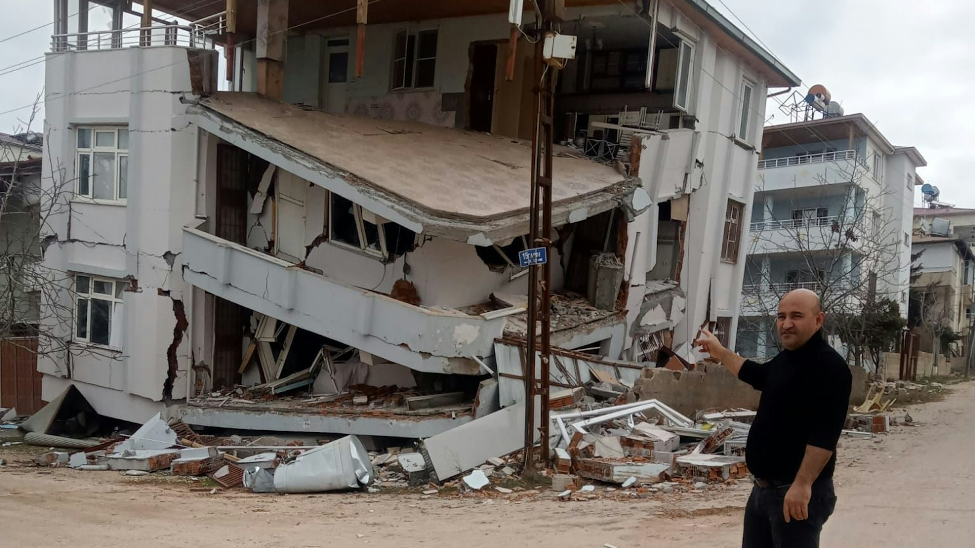 Ein Mann steht vor einem durch das Erdbeben in der Türkei zerstörten Haus.