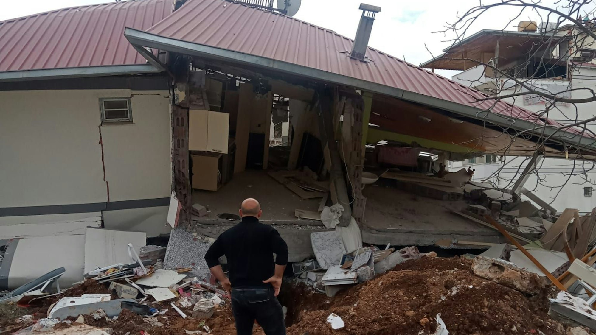 Ein Mann steht vor einem durch das Erdbeben in der Türkei zerstörten Haus.