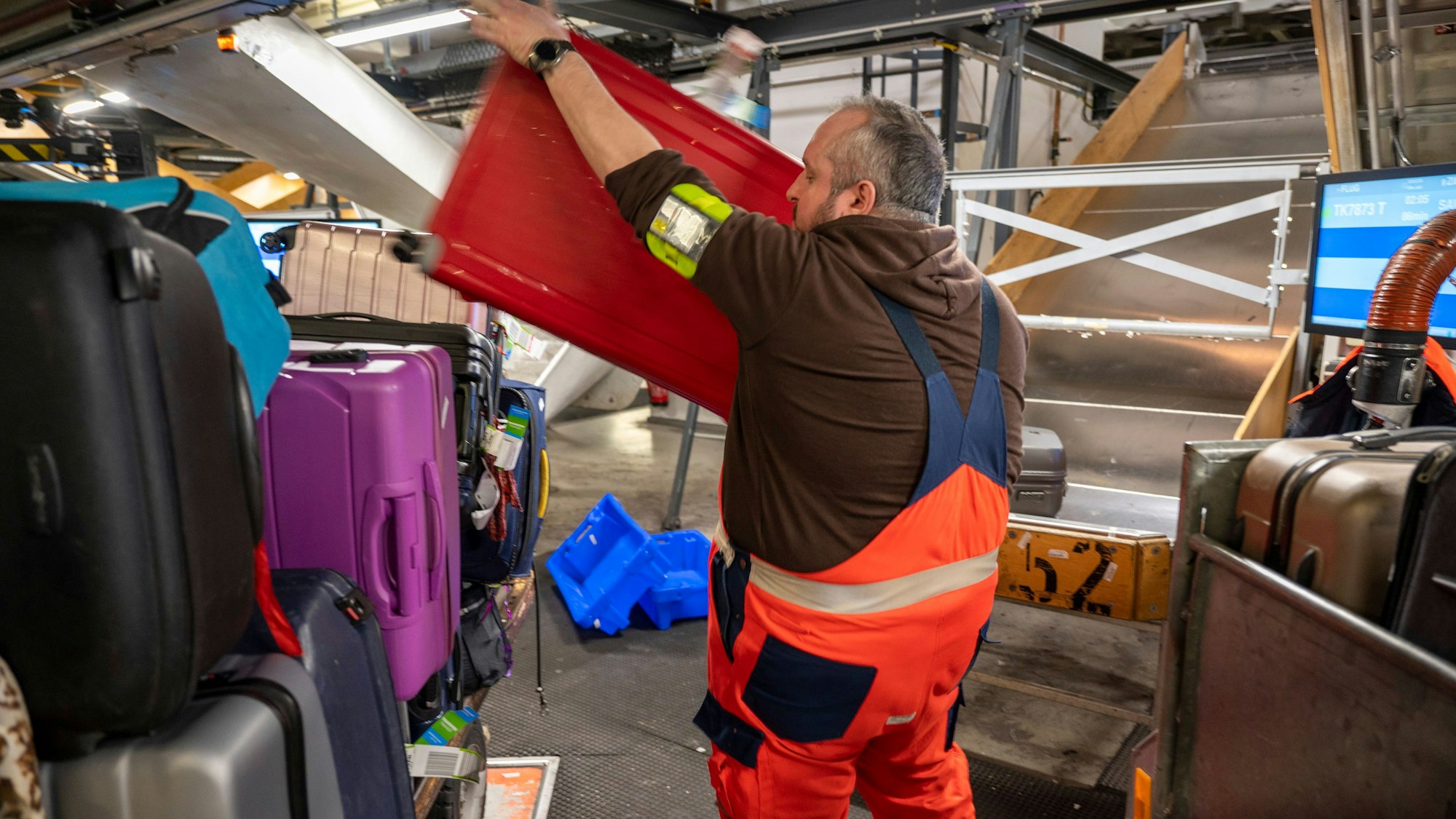 Ein Mitarbeiter der Gepäckabfertigung wuchtet einen roten Koffer auf einen Rollwagen.