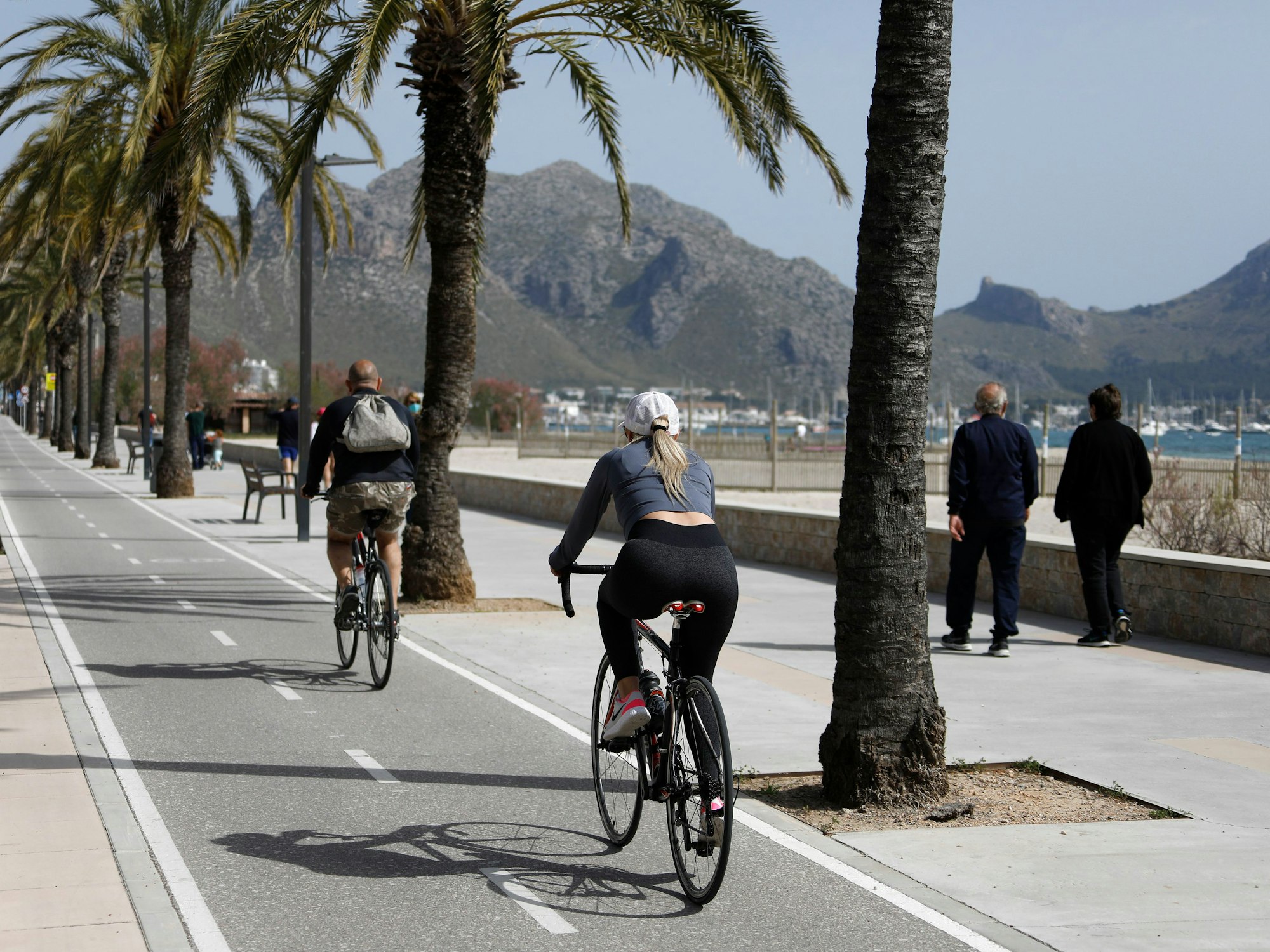 Menschen fahren im April 2021 am Hafen von Pollença auf der Insel Mallorca mit demFahrrad. Schon bald soll ein neuer Radweg das Zentrum von Mallorca mit dem Flughafen verbinden.