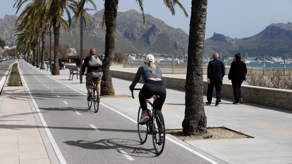 Menschen fahren im April 2021 am Hafen von Pollença auf der Insel Mallorca mit dem&nbsp;Fahrrad. Schon bald soll ein neuer Radweg das Zentrum von Mallorca mit dem Flughafen verbinden.