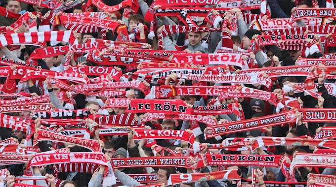 Fans des 1. FC Köln halten ihre Schals hoch.