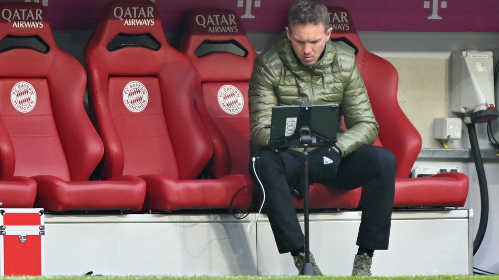 Bayern Münchens Trainer Julian Nagelsmann vom FC Bayern München sitzt auf der Trainerbank und schaut auf einen Bildschirm.
