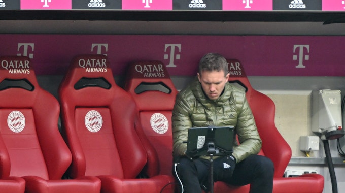 Bayern Münchens Trainer Julian Nagelsmann vom FC Bayern München sitzt auf der Trainerbank und schaut auf einen Bildschirm.