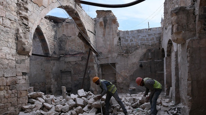Bauarbeiter stehen beim Wiederaufbau des Khabiya Markts im historischen Viertel Souk der Altstadt von Aleppo zwischen Trümmern eines zerstörten Gebäudes. (2019)