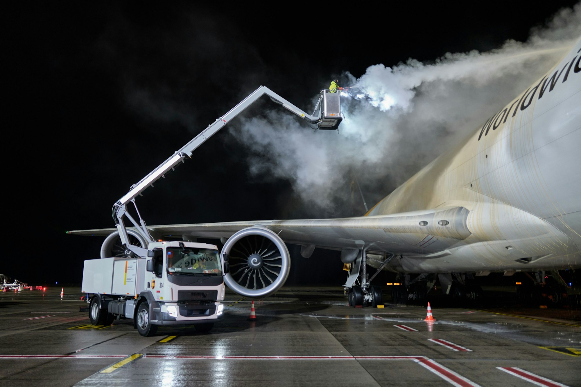 Eine Boeing-747 wird enteist. Das hellrosafarbene Chemikaliengemisch hüllt die Maschine kurzzeitig in hellen Nebel.