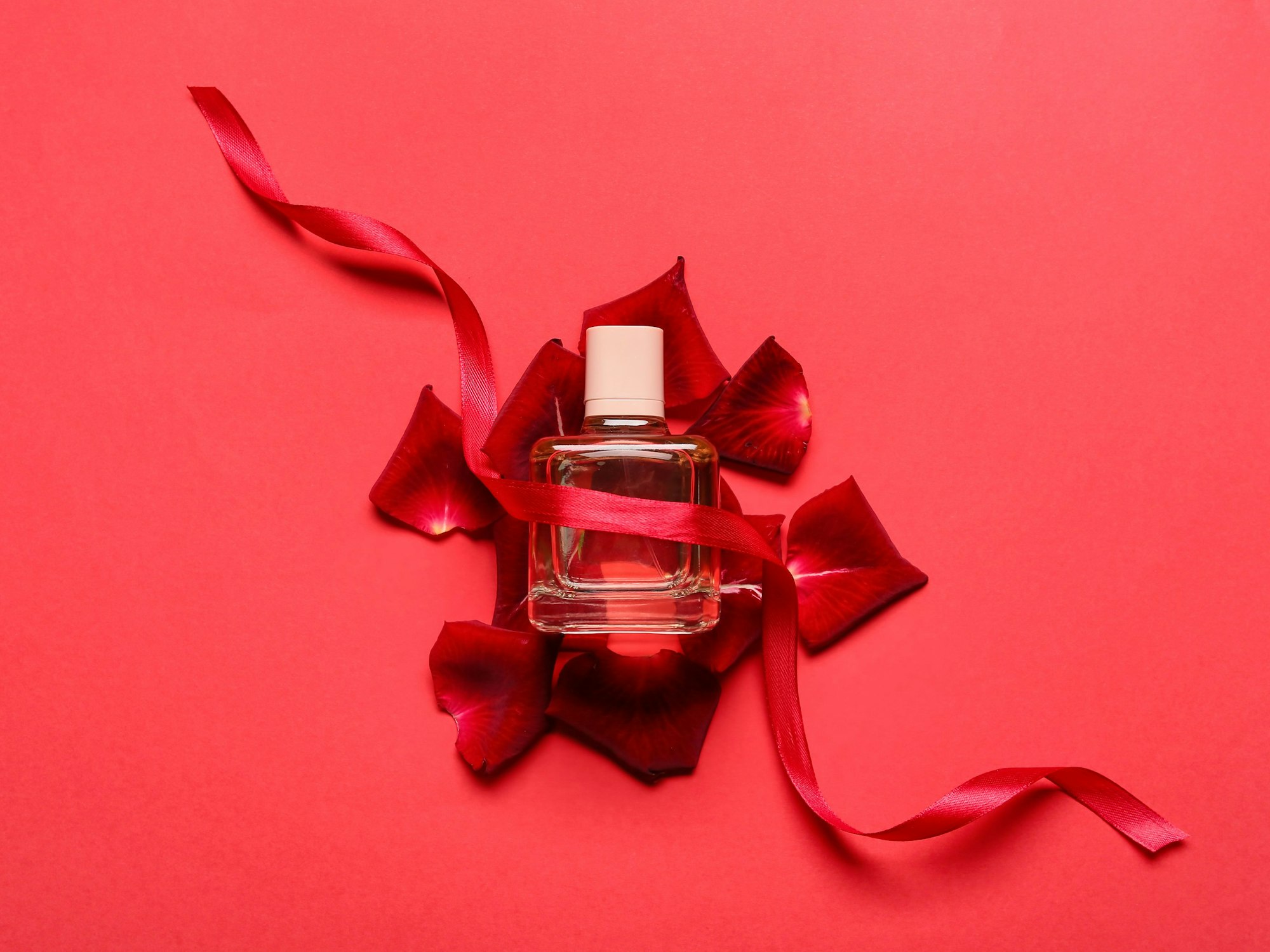 Eine Parfümflasche liegt auf roten Rosenblättern.