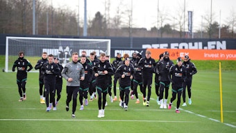 Die Spieler von Borussia Mönchengladbach laufen am 1. Februar 2023 gemeinschaftlich eine Runde auf dem Trainingsplatz-Rasen im Borussia-Park. Die Spieler tragen schwarze Gladbach-Trainingskleidung.