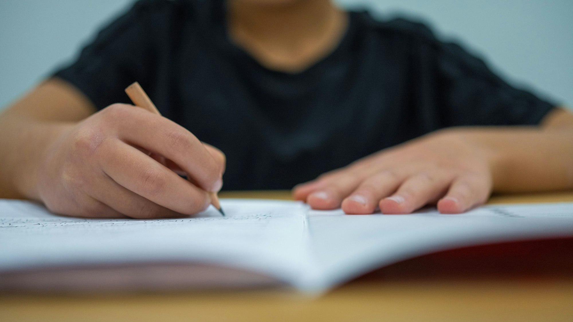 Ein Grundschüler sitzt an einem Tisch und schreibt mit einem Bleistift in sein Heft.