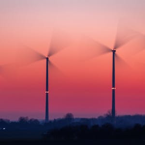 Die Rotoren von Windkraftanlagen drehen sich nach Sonnenuntergang. (Aufnahme mit langer Belichtungszeit)