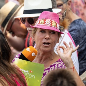 Andrea Kiewel, hier im „Fernsehgarten“, trägt einen rosa Hut auf dem Kopf.