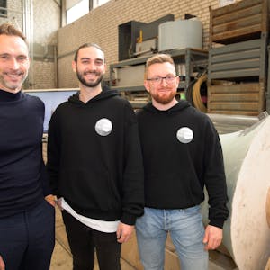 Köln-Business-Geschäftsführer Manfred Janssen mit Felix Roder und Marcel Heilich von „Rheinsharing“ stehen vor dem Prototyp des Kraftwerks. Sie lächeln in die Kamera.