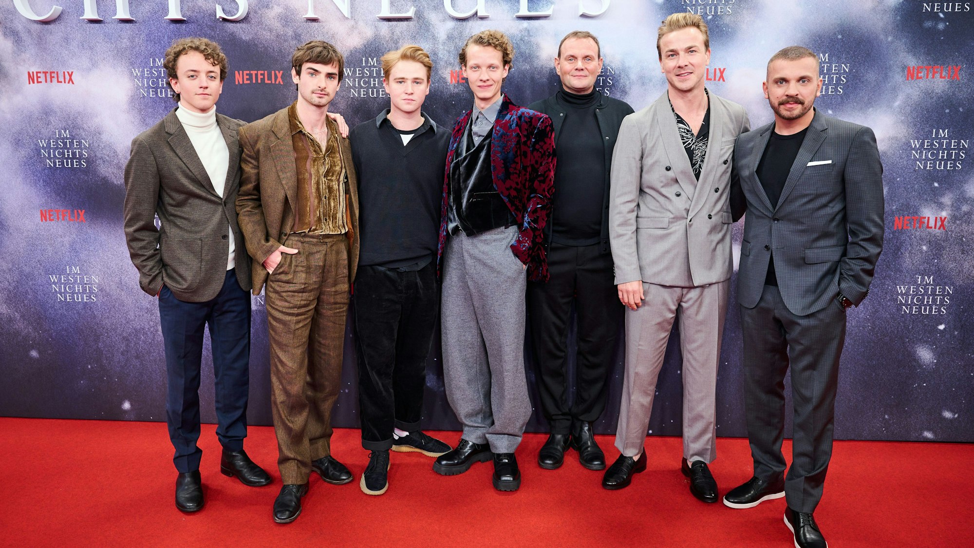 Sieben Schauspieler stehen auf dem roten Teppich.