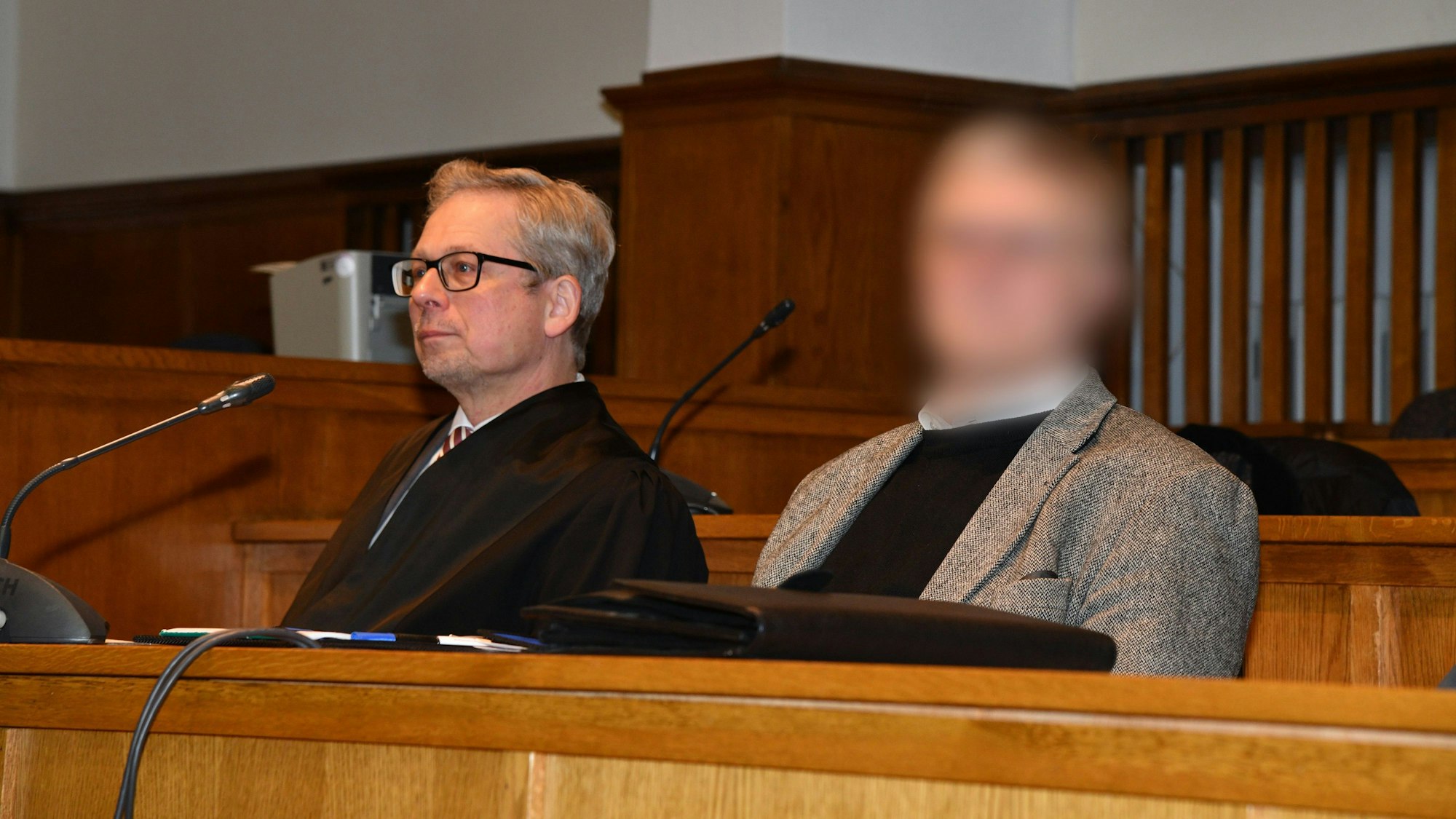 Ein Pfarrer (Gesicht gepixelt) sitzt neben seinem Anwalt im Gerichtssaal.