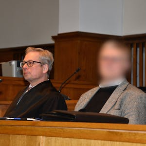Ein Pfarrer (Gesicht gepixelt) sitzt neben seinem Anwalt im Gerichtssaal.