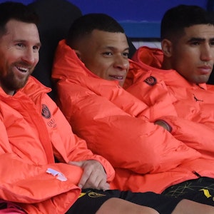 Lionel Messi, Kylian Mbappé und Achraf Hakimi sitzen nebeneinander auf der Auswechselbank.