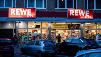 Die Leuchtreklame einer Rewe-Filiale in Köln leuchtet am Abend. An zwei Standorten in Köln testet Rewe ein neues Einkaufssystem.