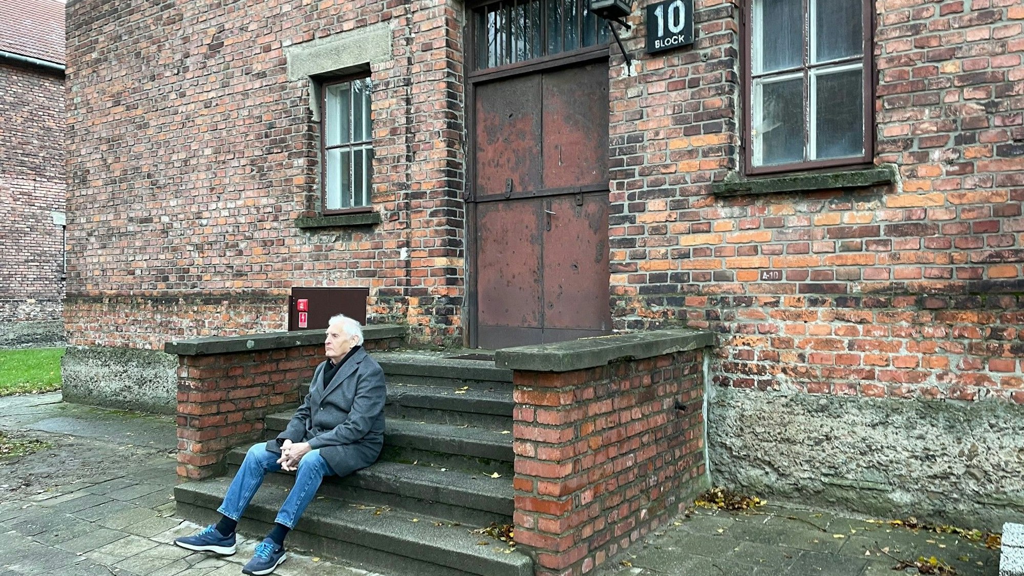 Dany Dattel sitzt auf der Treppe vor Block 10 im Stammlager Auschwitz.