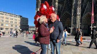 Brigitte und Klaus Beckmann mit roten Herzluftballons und dem Kölner Dom im Hintergrund.