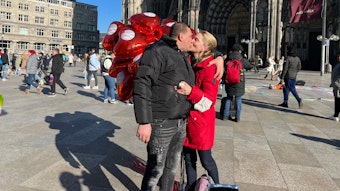 Susanne Shebeika und Abdullsalum küssen sich vor roten Herzluftballons auf der Domplatte.