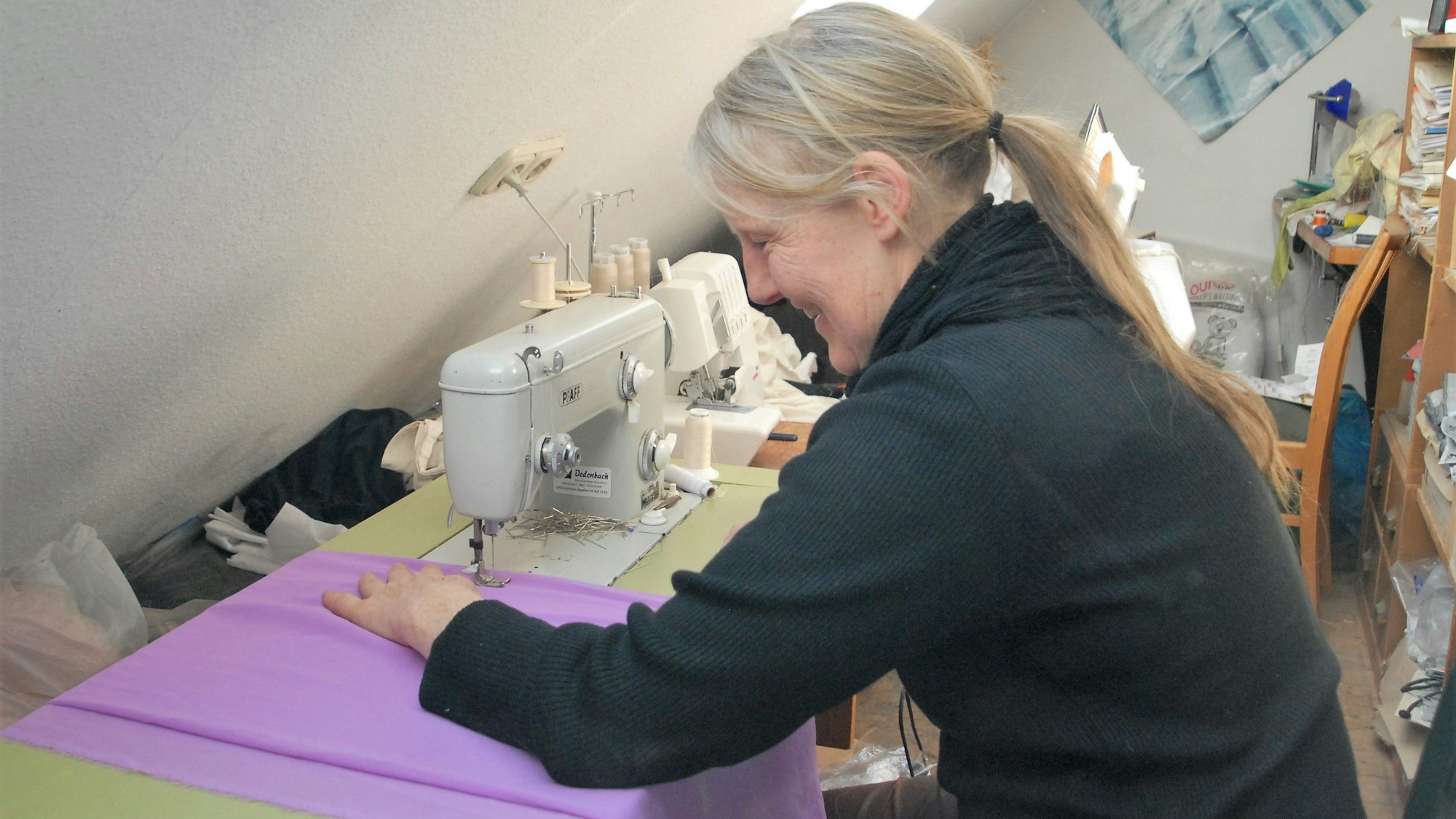 Das Foto zeigt Bekleidungsgestalterin Ursula Fischer. An ihrer Nähmaschine schneidert sie aus lila Stoff ein Kostüm.