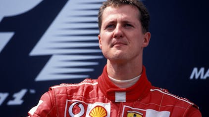 Der ehemalige Formel-1-Pilot Michael Schumacher schaut vor einem Werbebanner in die Ferne.
