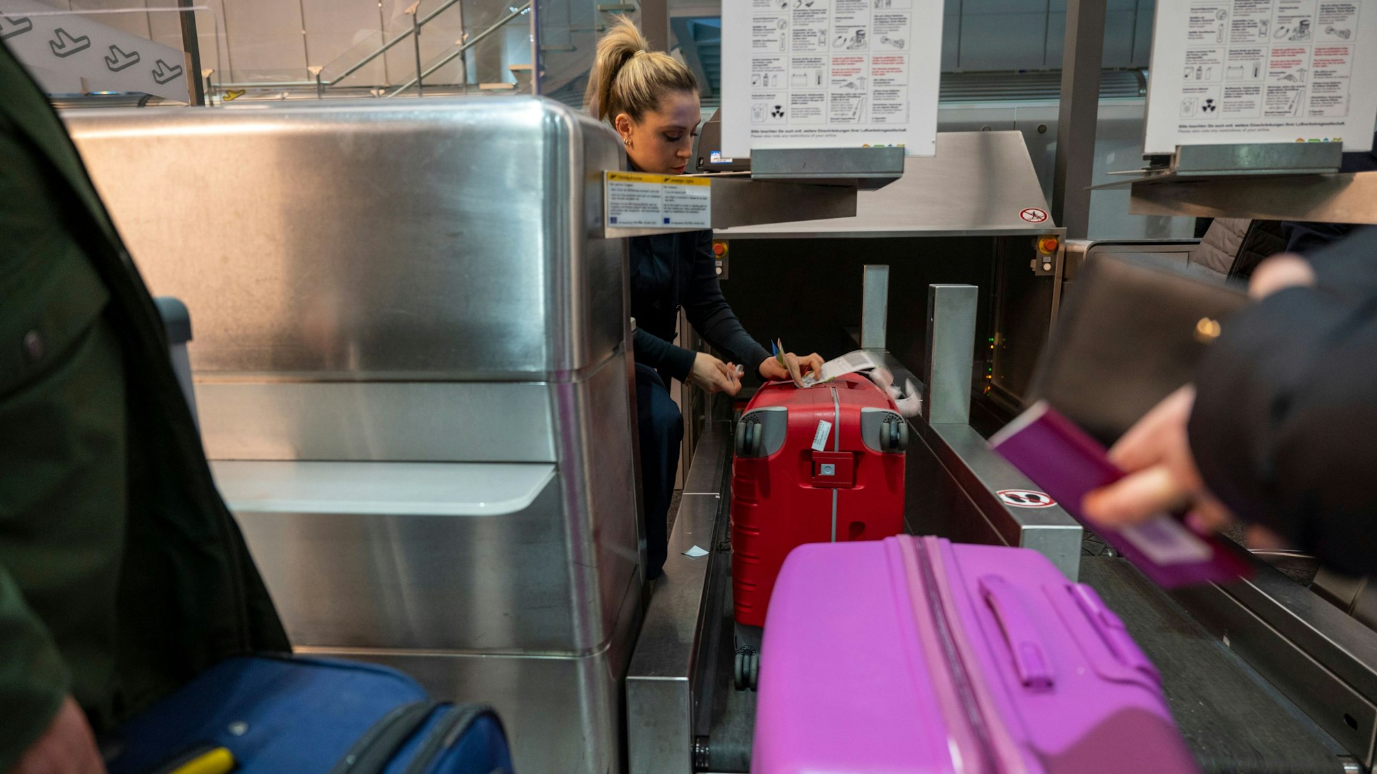 10.02.2023, Köln: Gepäckabfertigung beim Check-In. Am Flughafen Köln-Bonn darf auch nachts gestartet und gelandet werden. Koffer werden am Schalter über das Laufband geleitet, eine Mitarbeiterin befestigt das Gepäckband.