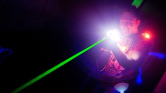 Ein Mann hat eine Waffe in der Hand, aus der ein grüner Laser schießt.