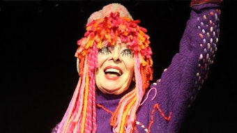 Eine kostümierte Frau mit Woll-Kopfschmuck lacht in die Kamera.