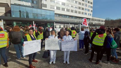 Klinikmitarbeiterinnen mit Schildern vor dem Klinikgelände