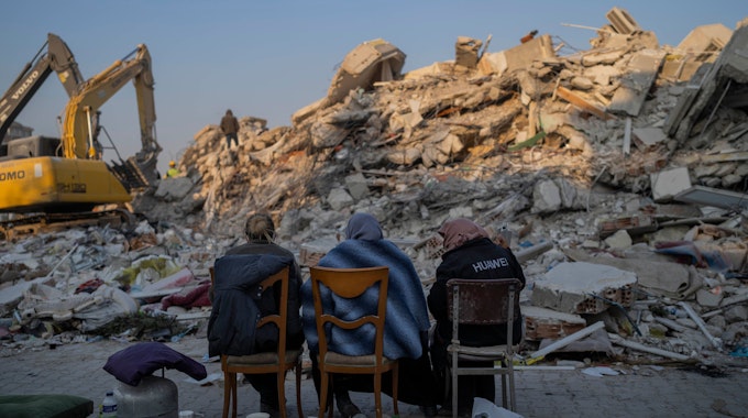 Frauen sitzen in Antakya vor Schuttbergen nach dem Erdbeben.
