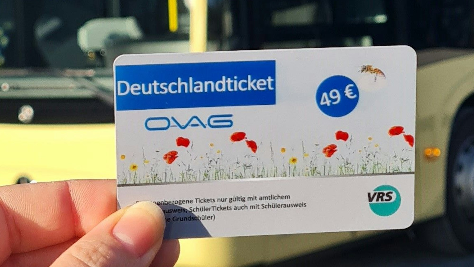 Eine Hand hält ein Tickets, im Hintergrund steht ein Bus.