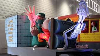 Ein Karnevalswagen zeigt einen Chrirurgen, der einen Handschuh mit der Aufschrift „Inflation“ anzieht und einer durch die Mangel gedrehten Figur mit der Aufschrift „Mittelstand“ in den Hintern schieben möchte.