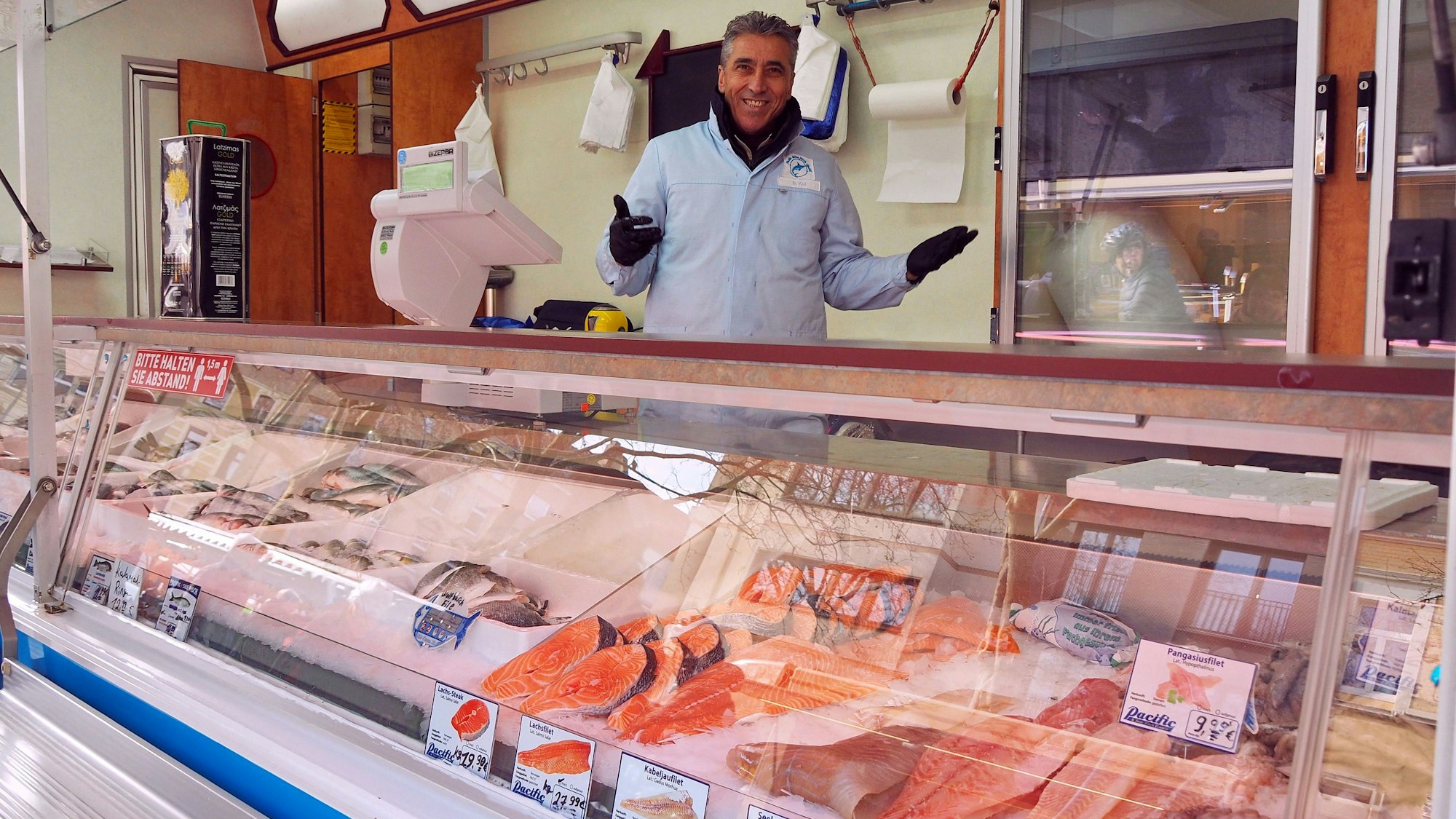 Der Inhaber steht mit ausgebreiteten Armen hinter seiner Fischtheke auf dem Wochenmarkt am Chlodwigplatz.