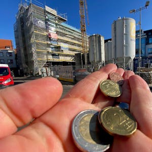 Eine Hand mit Münzen. Im Hintergrund sieht man die Baustelle des Brühler Rathaus. (Symbolbild)