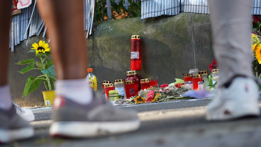 Zwei Menschen stehen vor einem Zaun, an dem mit Kerzen und Blumen eines von der Polizei erschossenen Jugendlichen gedacht wird. Im Fall um tödliche Polizeischüsse in Dortmund hat die Staatsanwaltschaft Anklage gegen fünf Polizisten erhoben.&nbsp;